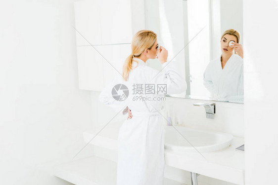 利用棉垫和照镜子的白浴袍中有吸引力的金发图片