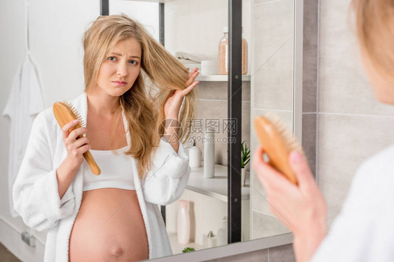 有毛发问题的不快乐孕妇在浴室里透过镜子看着图片