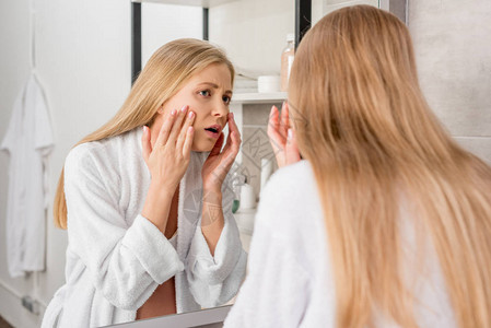 有皮肤问题的成年孕妇在浴室用镜子照面时看着她的脸部图片