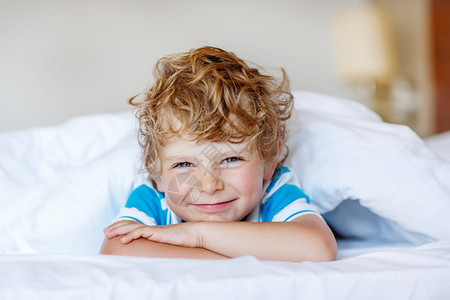 美丽快乐的孩子男孩睡在他的白色床上后快乐的小孩子在图片