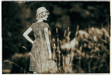1930年代时装服和草帽时装女郎与手提包站在农村风背景图片