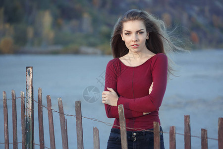 在日落时在木篱笆附近的岸边海滩上露天风寒的长着毛发的高加索年轻美女肖像图片