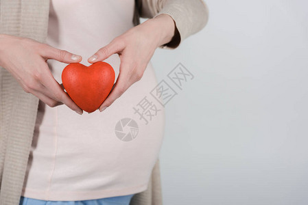 孕妇腹部和心脏被隔在灰色上的双手所孤立的近身剪图片