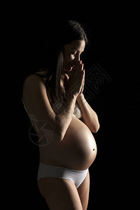 一位穿着白内裤的美丽孕妇的休眠在黑图片