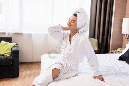 穿着白毛巾闭着眼睛的快乐女人和坐在酒店房图片