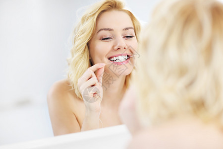 一张在浴室使用牙线的年轻快乐女照片图片
