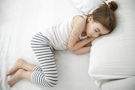 一个可爱的小女孩睡在白床上图片素材