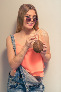 穿着夏衣和太阳眼镜的迷人女孩正在喝椰子奶图片