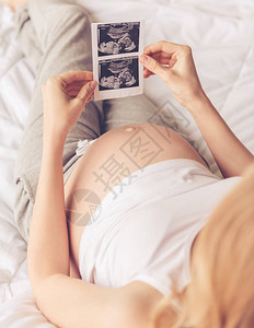 美孕妇坐在床上时持有声波图的剪裁图像图片