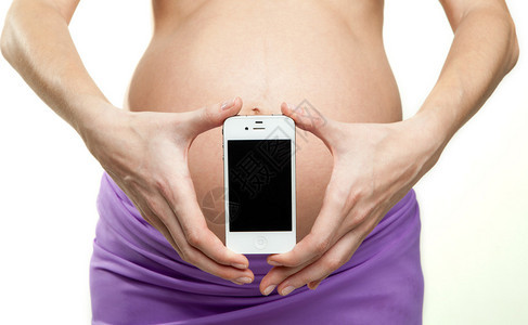 孕妇手中的手机以她的腹部为背景图片
