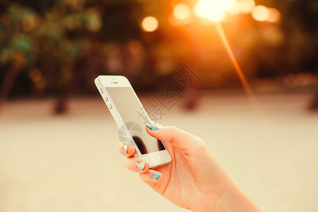 背景日落完美甲日光浴的女孩手持智能手机的特写图像黑屏手机短信视频通话海滨假期工作背景图片