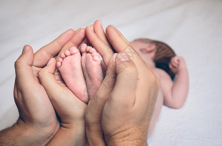 照片  |父母用手握着躺在床上的新生婴儿的脚照片  |一个美丽的快乐