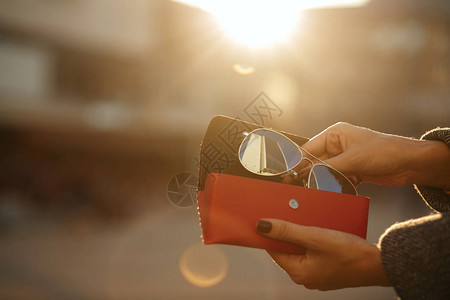 女手在太阳背景下打开红色眼镜盒的近距离镜头文本图片
