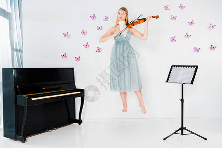 穿蓝裙子的漂浮女孩在钢琴附近拉小提琴用蝴蝶图片