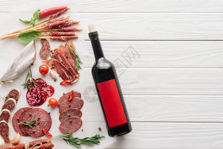 白色木制桌面上的红酒瓶和各种肉零图片