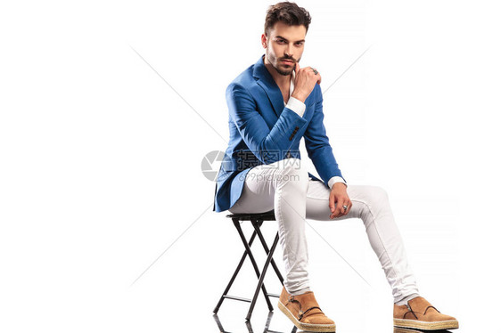 坐着的时尚男人用手指在白色背景上抚摸他的脸图片