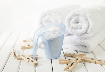 白色蓬松浴巾卷量杯中的洗衣粉和白板背景上的木制衣夹图片