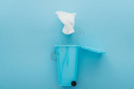白色折叠塑料杯倒在玩具垃圾桶底蓝色背景图片