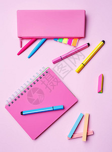女孩的桌面粉红色背景上的笔记本铅笔盒记号笔钢笔粉笔和松紧带图片