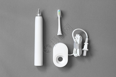 白色电动牙刷清洁刷子和灰色背景的充电器图片