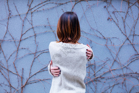 美丽的年轻美女拥抱着自己站在蓝色的墙壁上与植图片素材