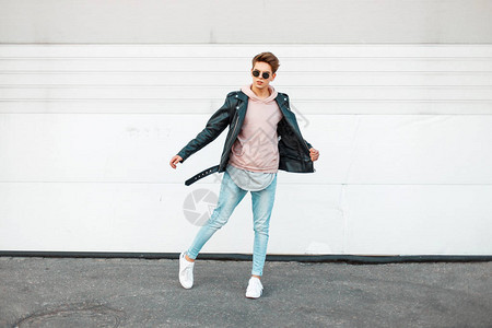 穿黑皮夹克的墨镜粉红色运动衫蓝品牌牛仔裤和白鞋的英俊图片