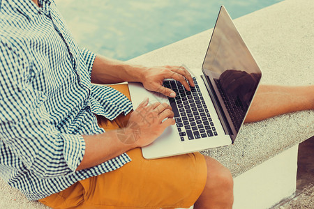 年轻人坐在码头上的海滩上用笔记本电脑工作发送邮件视频编辑和摄影在国外工作自由职业在线打字社交网络图片