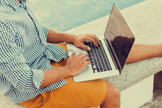 年轻人坐在码头上的海滩上用笔记本电脑工作发送邮件视频编辑和摄影在国外工作自由职业在线打字社交网络图片