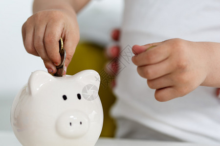 孩子的手把零钱硬币放入白色的存钱罐槽中预算费用概念使储蓄和有效的投资理念图片