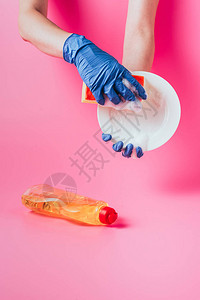 靠近洗碗液粉红色背景的橡胶手套洗涤盘中女清洁图片