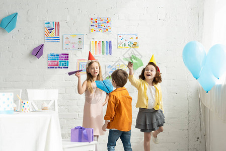 在家里的生日派对上玩纸机的可爱快乐小孩儿图片