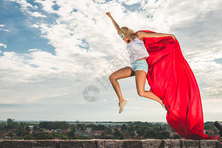 身穿红色连衣裙和红色斗篷的金发女郎在户外跳跃图片
