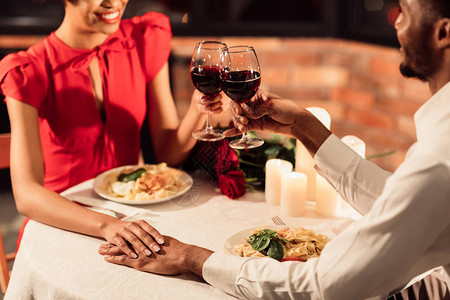 浪漫的约会晚宴无法辨认的非洲情人在餐厅桌上将玻璃手握在图片