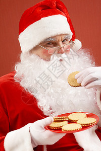 圣诞老人在吃饼干时用眼镜看着相机的照片图片