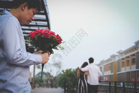 亚洲伤心欲绝的男人拿着一束红玫瑰在看到女人和另一个男人约会时感到悲伤心碎背景图片