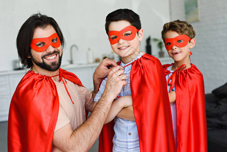微笑的父亲和儿子的肖像穿着红色超级英雄服装在图片