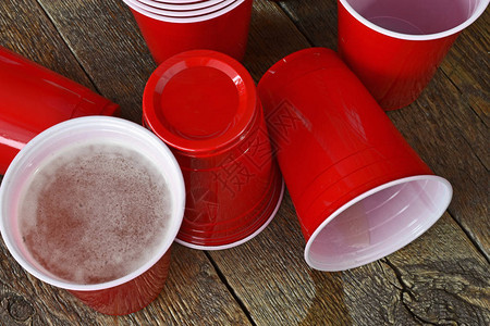 一张红色塑料杯的近距离图像在旧酒吧桌子上放着洒满啤图片