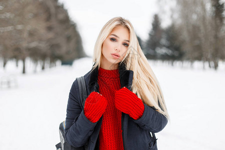 穿一件优雅的冬大衣穿着红色时装编织毛衣的漂亮年轻女模特在下雪的图片