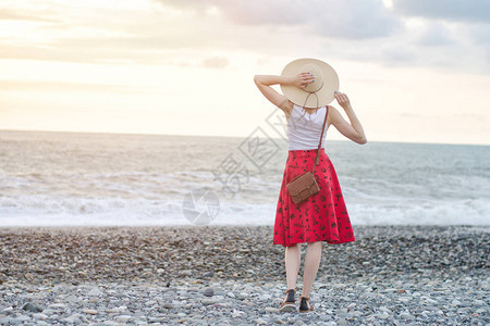 穿着红裙子的女孩和帽子站在海边日图片