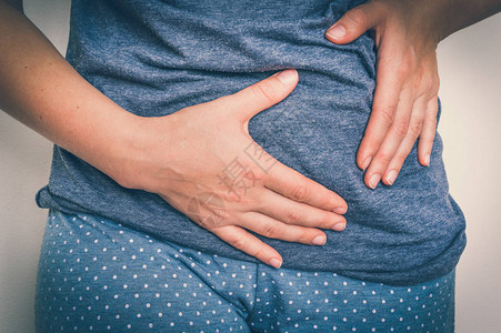 胃痛的女人抱着她的肚子疼身体疼痛概念图片