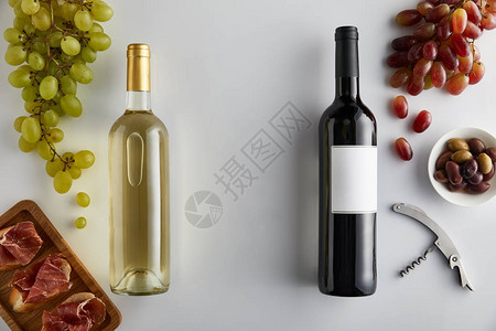 白色背景的长棍面包上的葡萄开瓶器橄榄和切片意大利熏火腿附近装有白葡萄酒和红葡萄酒的瓶背景图片