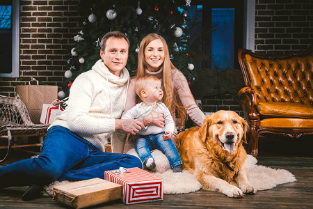 父亲妈和孩子一岁的白种女人坐在圣诞树旁边的地板上图片