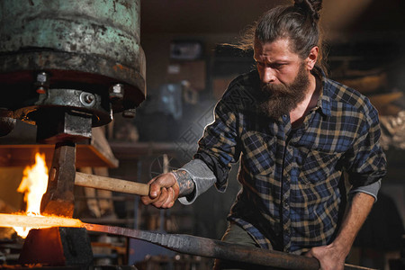 真正的残酷的铁匠在一个车间用红热铁制成的机械锤里工作图片