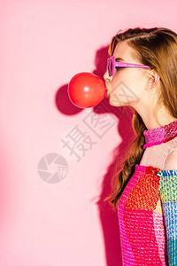 戴墨镜的漂亮女孩在粉红色上吹红色泡糖图片