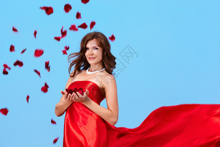 穿着优雅的红礼服拿着玫瑰花瓣的图片