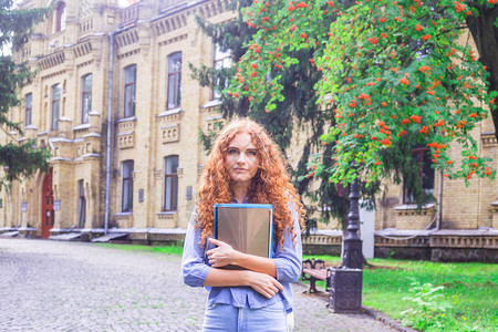 大学旁边手里拿着文件夹和教材的红发女学生回到学校的概背景图片