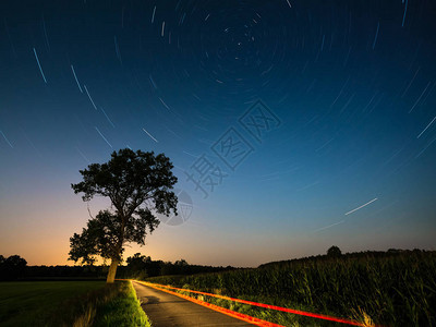 星轨与北半球和星的夜景漩涡夜曝光车灯照亮的夜光乡间小路图片