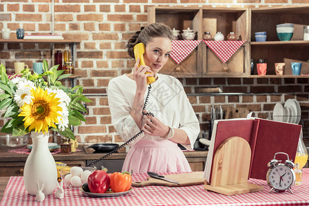 漂亮的成年家庭主妇在厨房准备饭菜时通过电话交图片