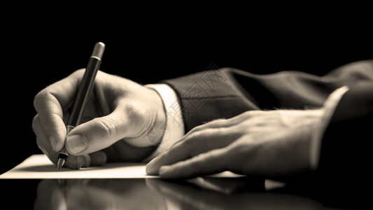 一位身穿西装的商人在完成商业交易或敲定合同或协议时用钢笔签署文件的特图片