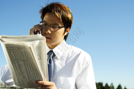 商人在打电话时看金融报纸同时图片
